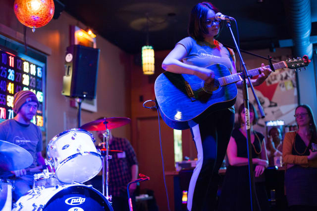 Musician performing with an acoustic guitar at the Love Bomb 2017 event, accompanied by a drummer, with attendees enjoying the live music in a vibrant venue.